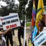 A group of protesters engaged in a tense debate over Diversity, Equity, and Inclusion (DEI) policies. On one side, individuals hold signs opposing affirmative action, with slogans like 'Stop Discriminating on the Basis of Race.' On the other side, activists display signs advocating for diversity, opportunity, and justice, alongside flags representing various social movements, including Black Lives Matter and LGBTQ+ rights. The scene captures the deep political and ideological divide over DEI initiatives in the United States